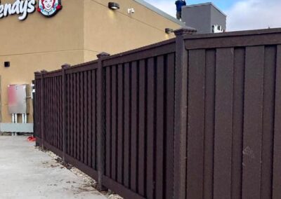 A tall brown fence runs along the side of a Wendy’s restaurant; a person stands on the roof near the edge, with a cloudy sky in the background.