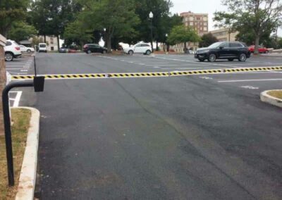 A nearly empty parking lot with a yellow and black striped barrier arm across the entrance, several trees in the background, and a few parked cars visible.