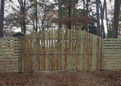 A wooden fence with a gate blends in seamlessly with the surrounding fence, making the entrance nearly invisible. Tall trees and autumn leaves are visible in the background.